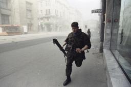 A soldier runs down a smoky, empty street. 