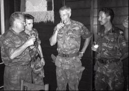 Four men wearing camouflage military uniforms stand together, holding drinks.