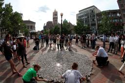 People in a town square stand and kneel around a large display of coffee cups laid out on the ground.