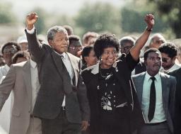 A man and a woman, raising their fists in a sign of victory, followed by a large crowd.