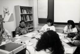 A group of women sit around a table covered in papers.