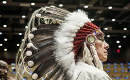A man wearing an eagle feather headdress in a hall. 