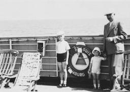 A man in a suit poses with two children against the railing of a ship.