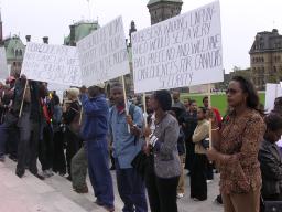 A crowd of protestors holding signs on the steps of Parliament.