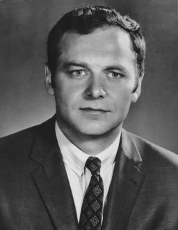 Black and white headshot of a man wearing a suit and tie. 