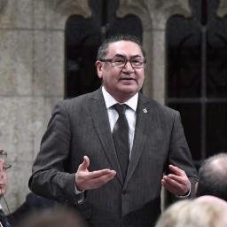 A man wearing a suit stands and speaks in the House of Commons.