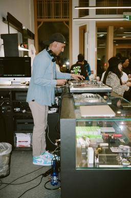 Suraj, a DJ wearing a baseball cap backwards, spins records on a glass counter at an event. 