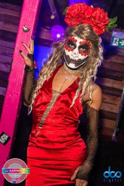 A drag queen with long wavy blond hair topped with large red roses, painted face and red satin dress.