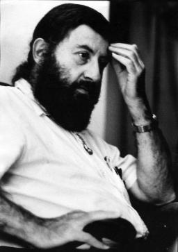 Black-and-white photo of a bearded man holding his hand up to his forehead. 