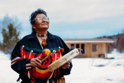 A person wearing a colourful robe gazes upward while playing a hand drum.