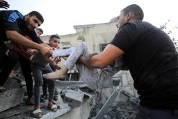 Men wearing black shirts lift the body of a child from rubble.