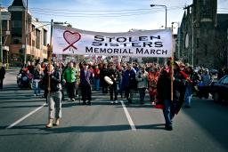 Two women hold a large banner that reads “Stolen Sisters Memorial March” as they lead a large group of demonstrators down a city street.