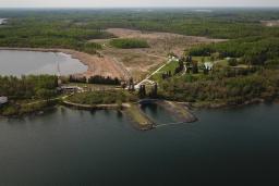 An aerial shot of a community surrounded by water and forest, with a road arcing away from the water and through the trees.