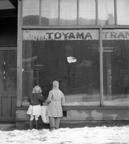 Black-and-white photograph of two children looking into an abandoned store window.