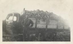 A young man poses in front of a transport truck full of sugar beets.