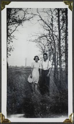  A young woman and a young man pose in a field with trees in the background.