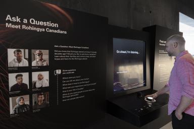 A man touches a large button in front of a video screen that displays the words, "Go ahead, I'm listening." In the foreground, there is a panel with photos of six people under a title that reads, "Ask a Question, Meet Rohingya Canadians." 