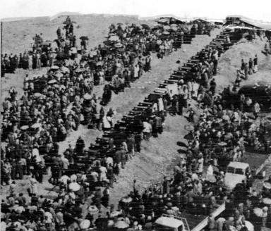 Aerial photo of a long line of coffins surrounded by a large crowd of people. 