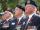 Three older men in Canadian Legion uniforms sit beside each other. They are all wearing Remembrance Day poppies on their uniforms.