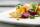 Bright gold-coloured potato wedges are artfully arranged on a square white plate, along with leaf greens, wedges of red beets, and garnish.