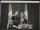 A black and white photograph of Nelson Mandela standing in front of a podium. He is smiling and waving.