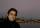 Close-up of a smiling man at dusk. Behind him is a body of water and on the other side there are boats, lights and buildings.