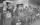A line of miners hold lunch pails as they punch a time clock.