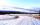A snow-covered country road with mountains in the background.