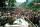 Two uniformed soldiers sit on a large vehicle, overlooking a densely packed crowd of people that stretches into the distance.