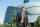 A person standing with the Museum in the background. He is wearing a suit, smiling, with his right hand in his pocket, looking directly at the viewer.