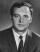 Black and white headshot of a man wearing a suit and tie.