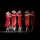 On a dark stage are five ballet dancers dressed in red knee-length flowy costumes with white square-like hats. They are looking forward with their hands in prayer.