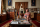 A woman kneels beside a coffee table surrounded by books and heirlooms.