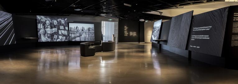 A museum gallery featuring photographs projected onto large screens with seating in the middle of the room. Partially obscured.