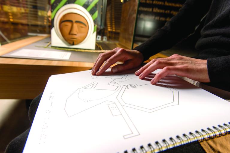 A person’s hands are reading braille on a page of a ring binder notebook with geometric designs. Partially obscured.