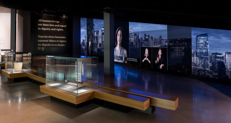 A gallery with exhibit display cases and visitor benches. Partially obscured.