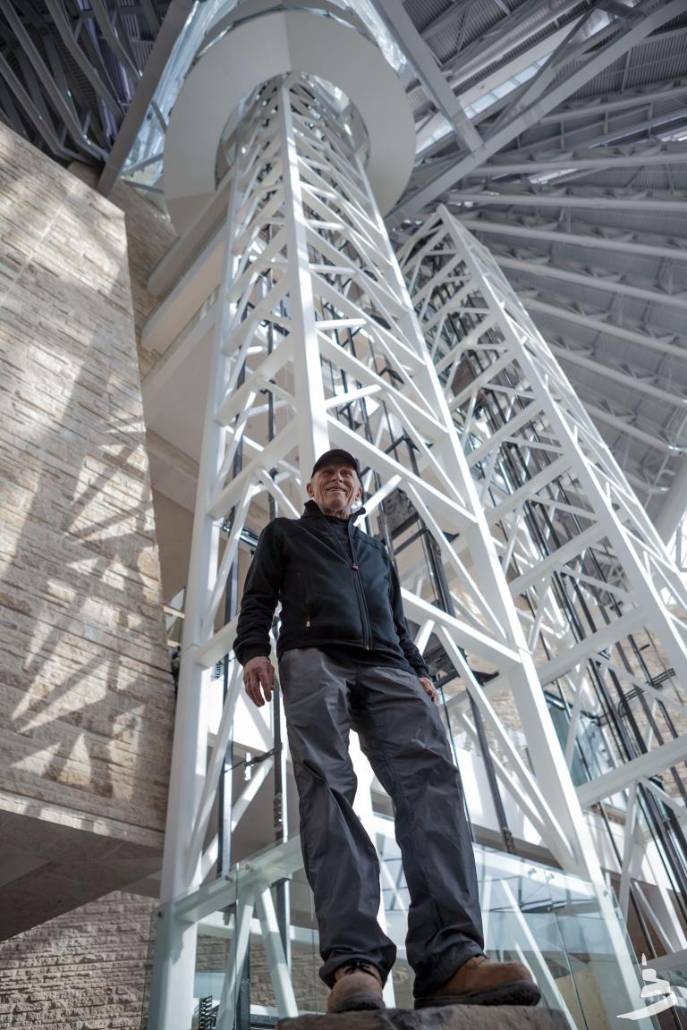 Antoine Predock, the architect of the Museum, is pictured inside the Museum from a low angle with white beams rising above him.