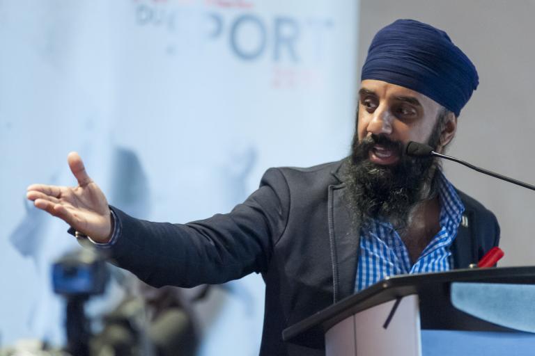 A head-and-shoulders image of Pardeep Singh Nagra speaking into a microphone at a podium. He is looking to his right and his right arm is extended out with his palm upturned.