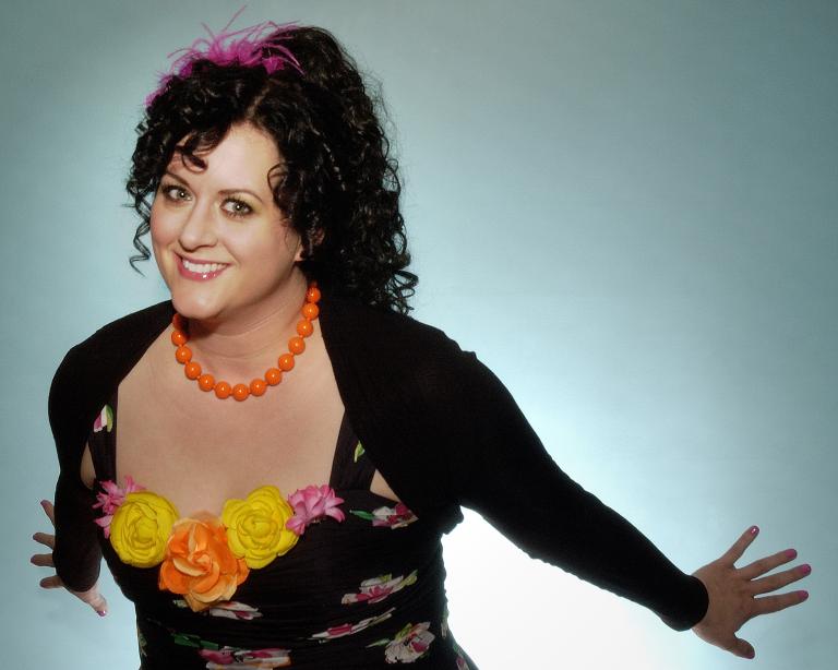 A smiling woman with her arms extended behind her Partially obscured.