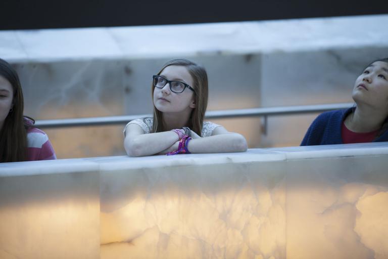  Three young people leaning on a glowing alabaster ramp and looking up. Partially obscured.
