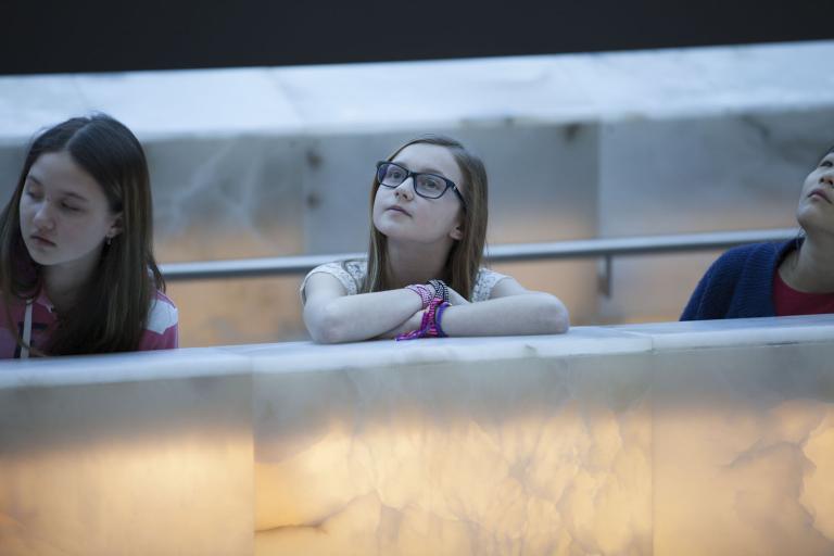 Two young girls lean on a glowing stone wall and look upward. Partially obscured.