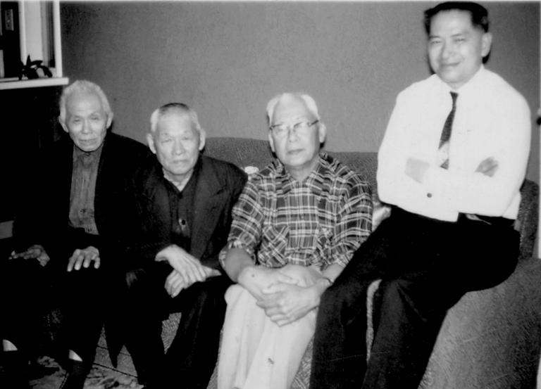 Four men sitting on a couch looking at the Camera. Partially obscured.