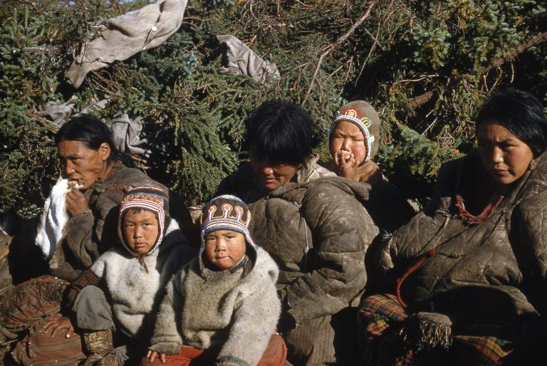 A group of women and children sitting together. The two children in the front are looking at the camera. Partially obscured.