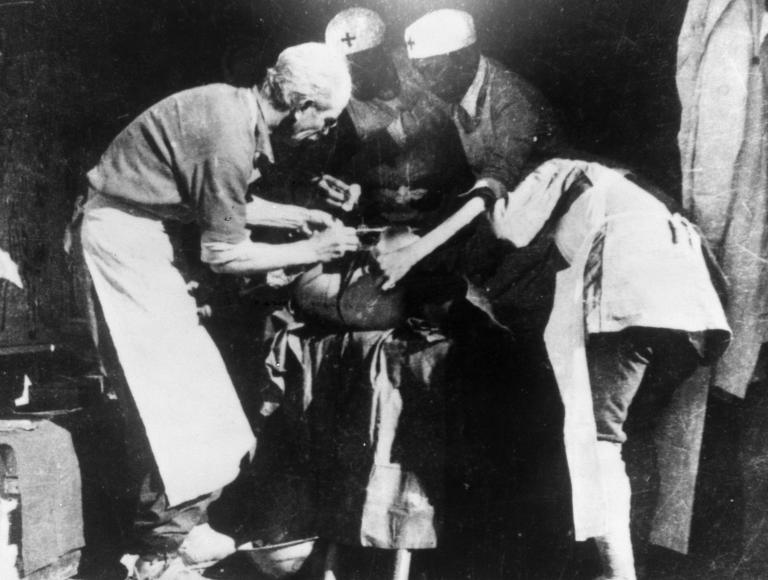 Four people standing around an operating table. Partially obscured.