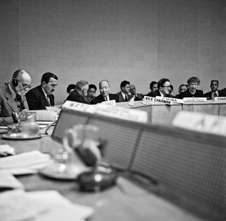 Black and white archival photo of a group of people sitting around a conference table.