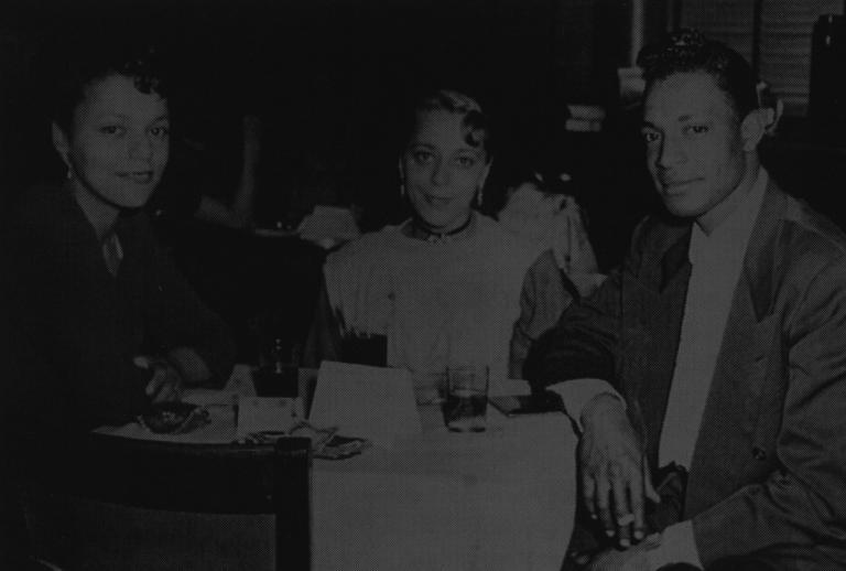 A black and white photo of Viola Desmond (centre) at a club with her sister and brother-in-law (1955). Partially obscured.