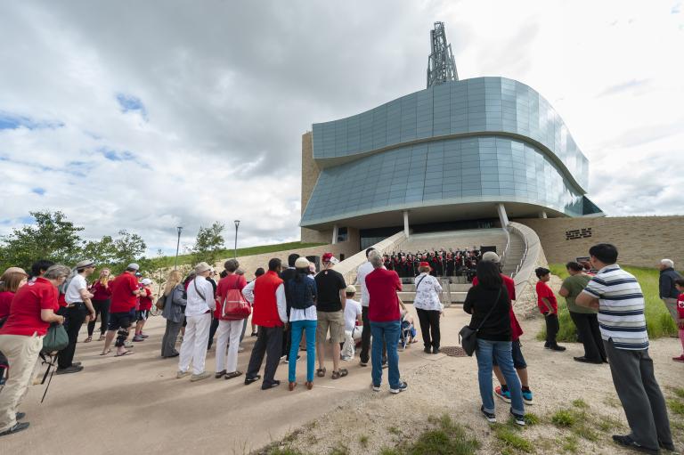 A group of people watching a choir as they perform on the Museum’s exterior amphitheater. Partially obscured.