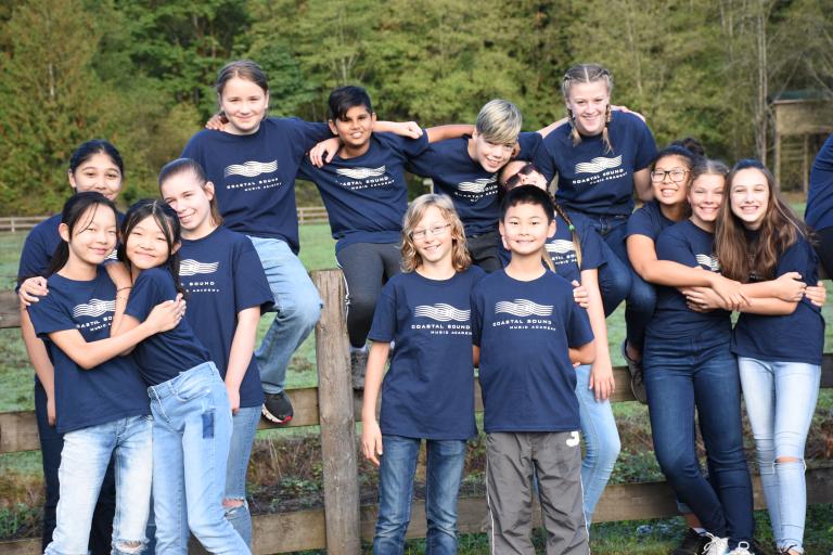 A group of youth outside on a wood fence, posing for the camera with their arms around one another. Partially obscured.