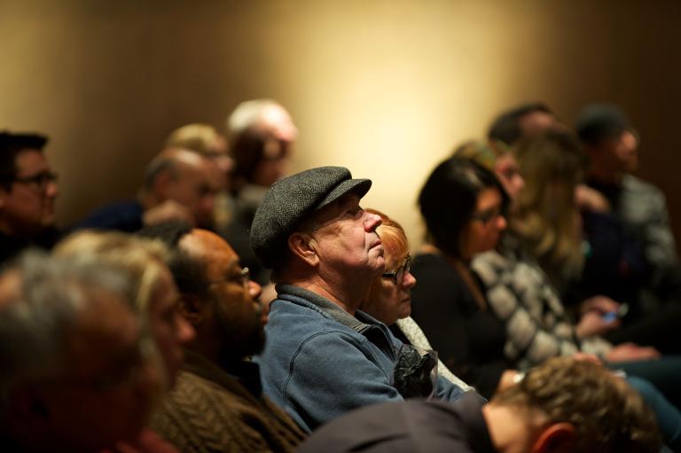 People sitting in an audience. Partially obscured.