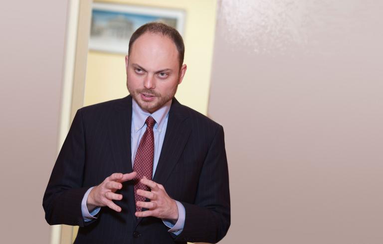 A man speaking with his arms bent at the elbows and hands held up facing each other. Partially obscured.